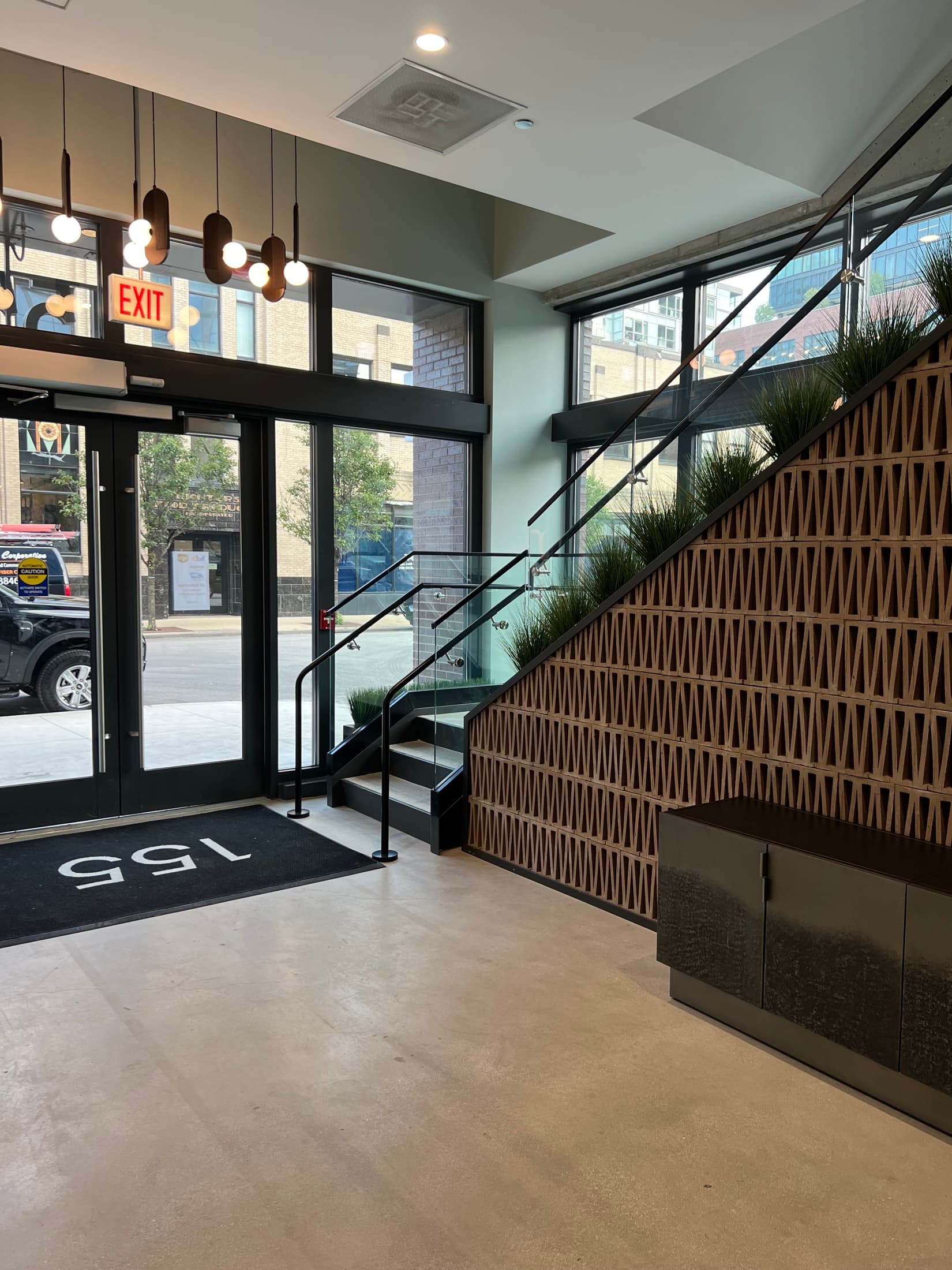 Lobby stair with a black steel and glass railing beside a sculptural perforated-wood screen wall with integrated planters.