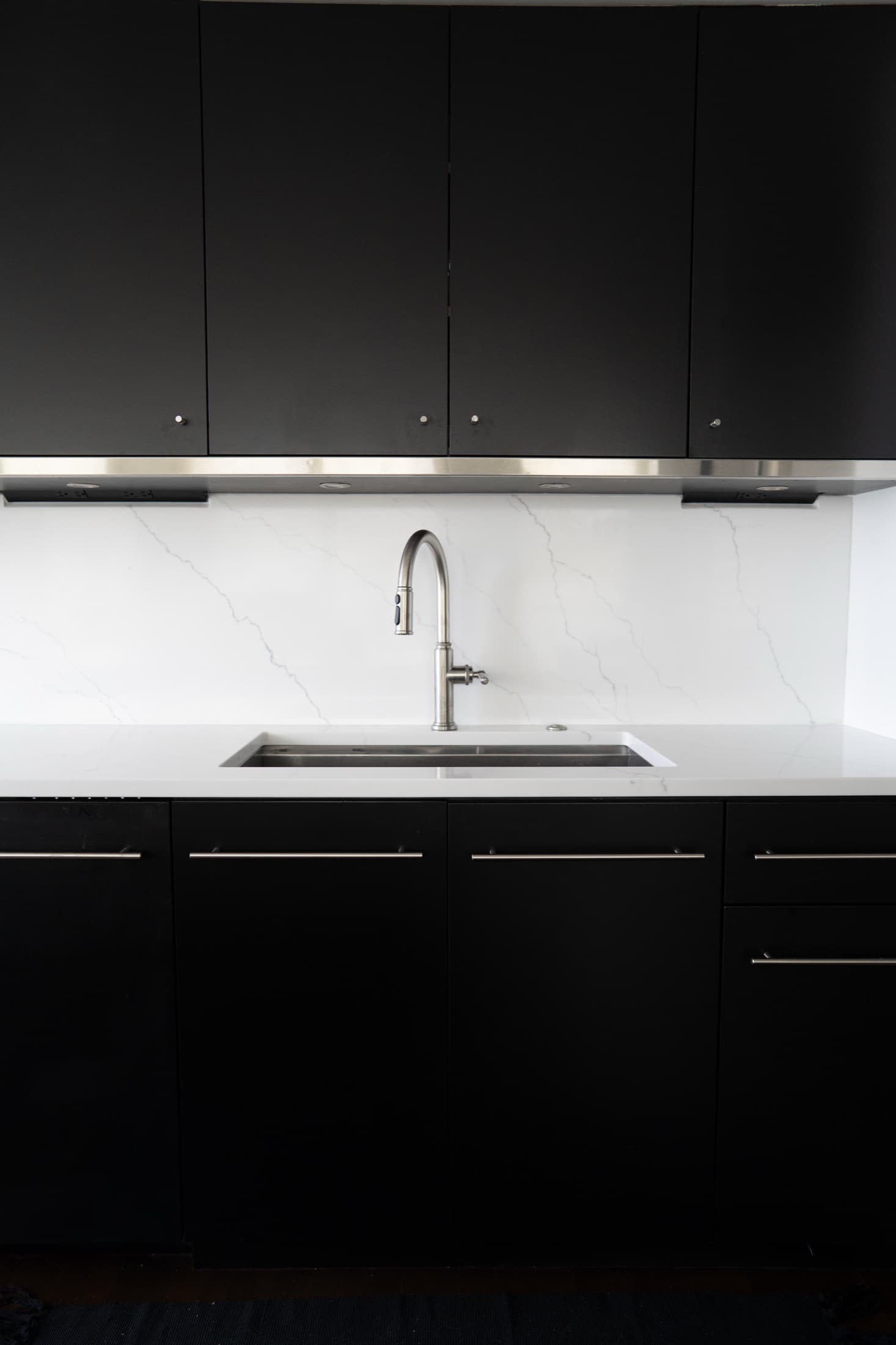 Matte-black cabinetry with a bookmatched Calacatta marble backsplash, undermount sink, and stainless pull-down faucet.